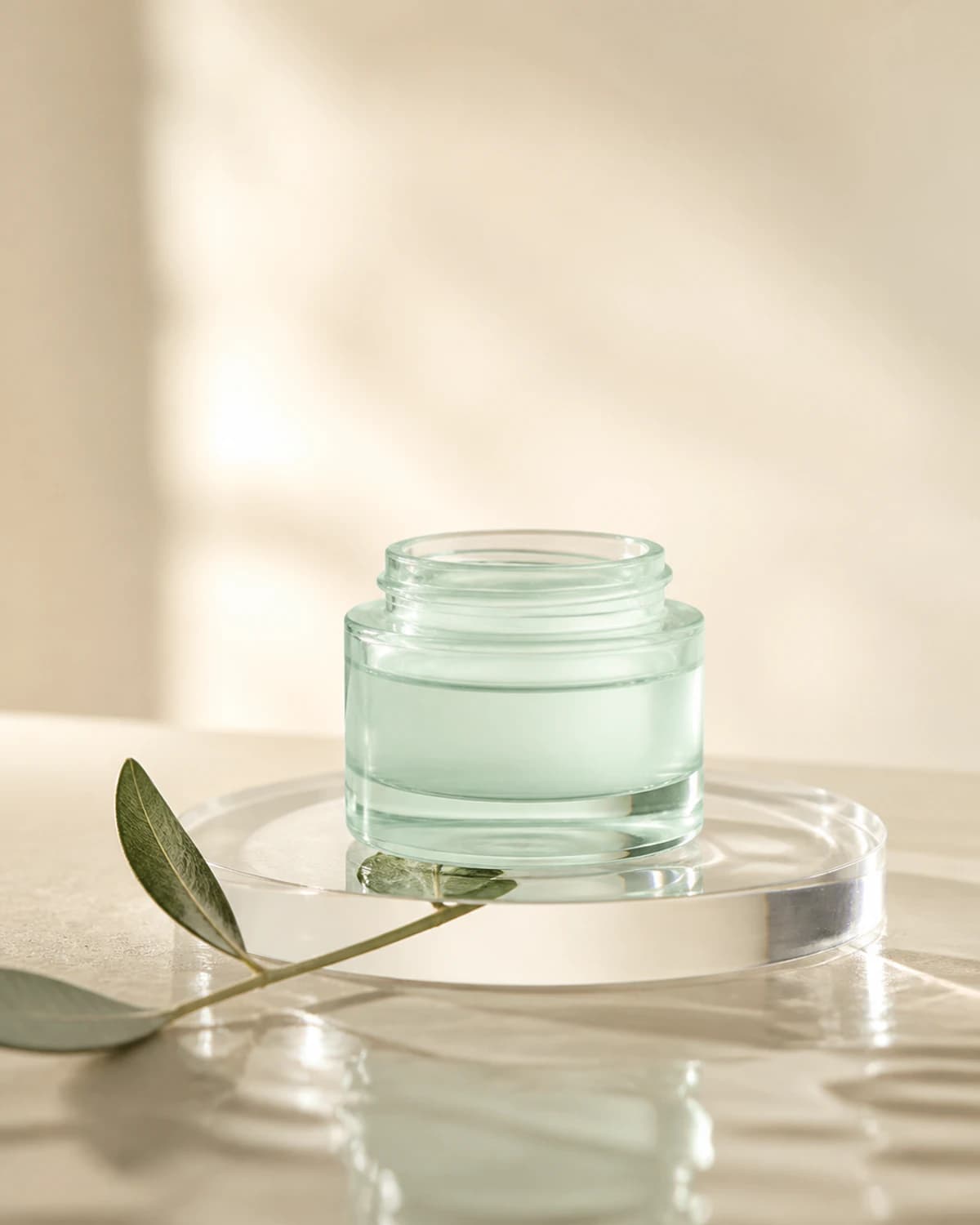 Bright product composition with a pale-mint glass skincare jar and leaf